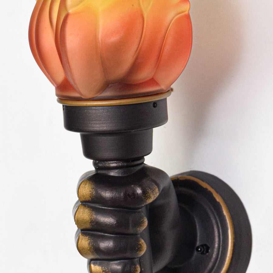 Close view of decorative wall sconce with orange flame glass shade and detailed black metal holder showcasing antique style lighting design.
