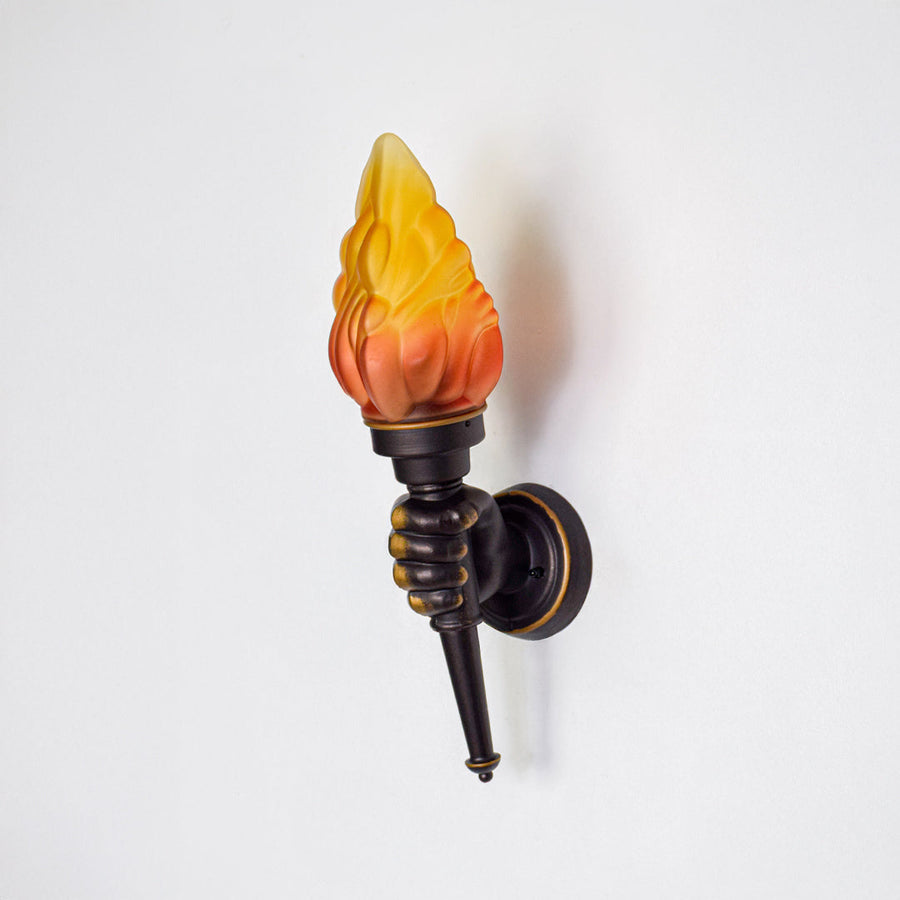 Rustic wall sconce with flame style glass shade and black metal frame on neutral background perfect for vintage home decor lighting.
