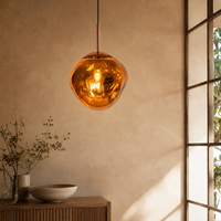 A modern pendant light with a textured, hammered copper-colored glass globe shade hanging in a warm, minimalist room with a beige wall and a window frame on the right.