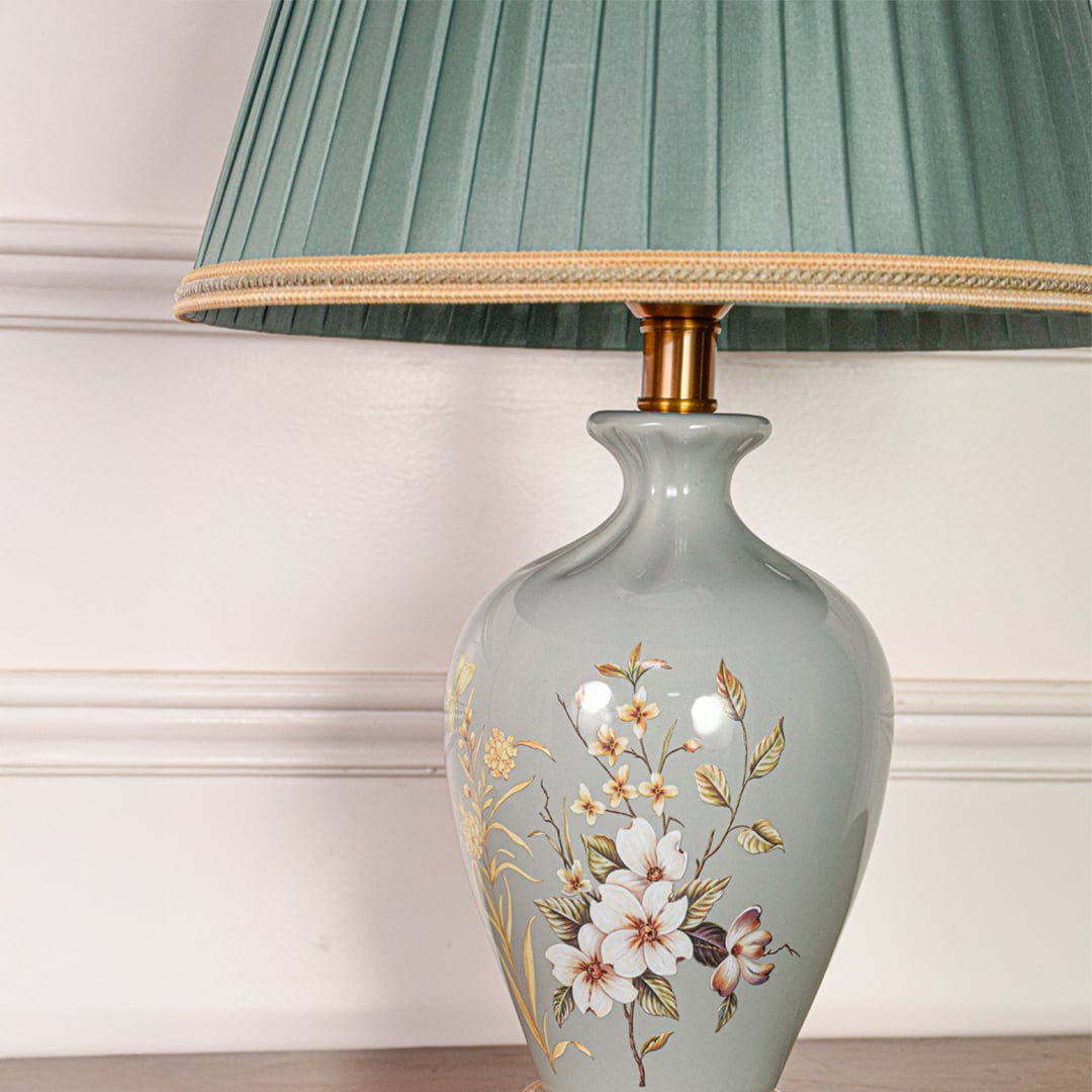Closeup of sage green ceramic table lamp showing delicate hand painted floral details smooth glaze and gold metal base.