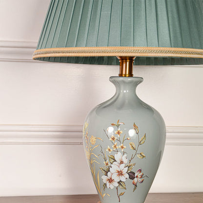 Closeup of sage green ceramic table lamp showing delicate hand painted floral details smooth glaze and gold metal base.