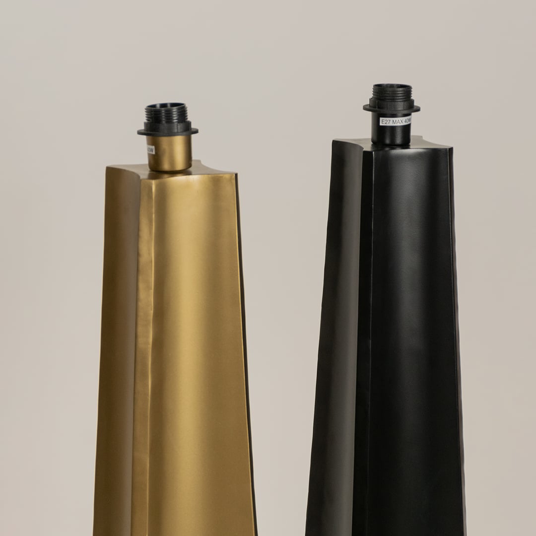 Close up of two tall floor lamp bases one in gold and one in black with tapered shapes and exposed bulb sockets shown against a neutral background.