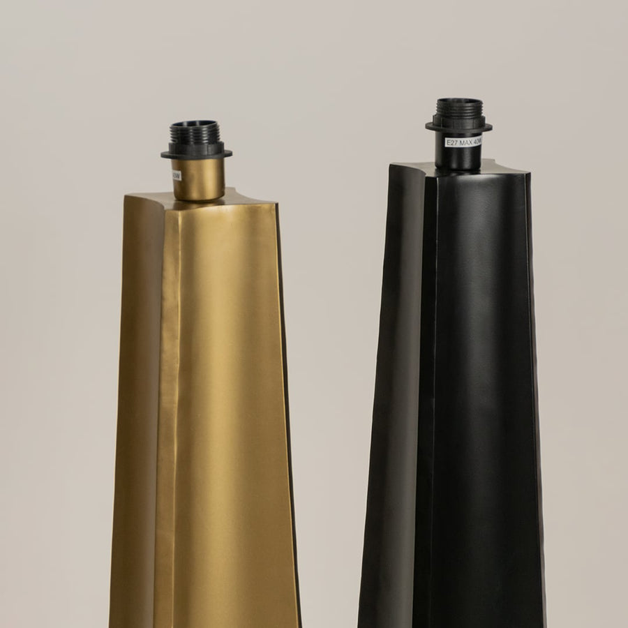 Close up of two tall floor lamp bases one in gold and one in black with tapered shapes and exposed bulb sockets shown against a neutral background.