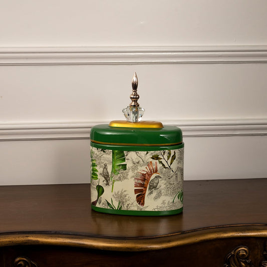 Green tropical jar with golden lid and crystal finial featuring detailed tropical leaves on white background.