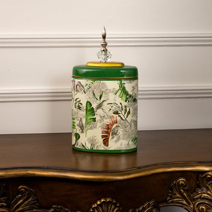 Green tropical decorative jar with gold accent and crystal top featuring botanical design on white background.