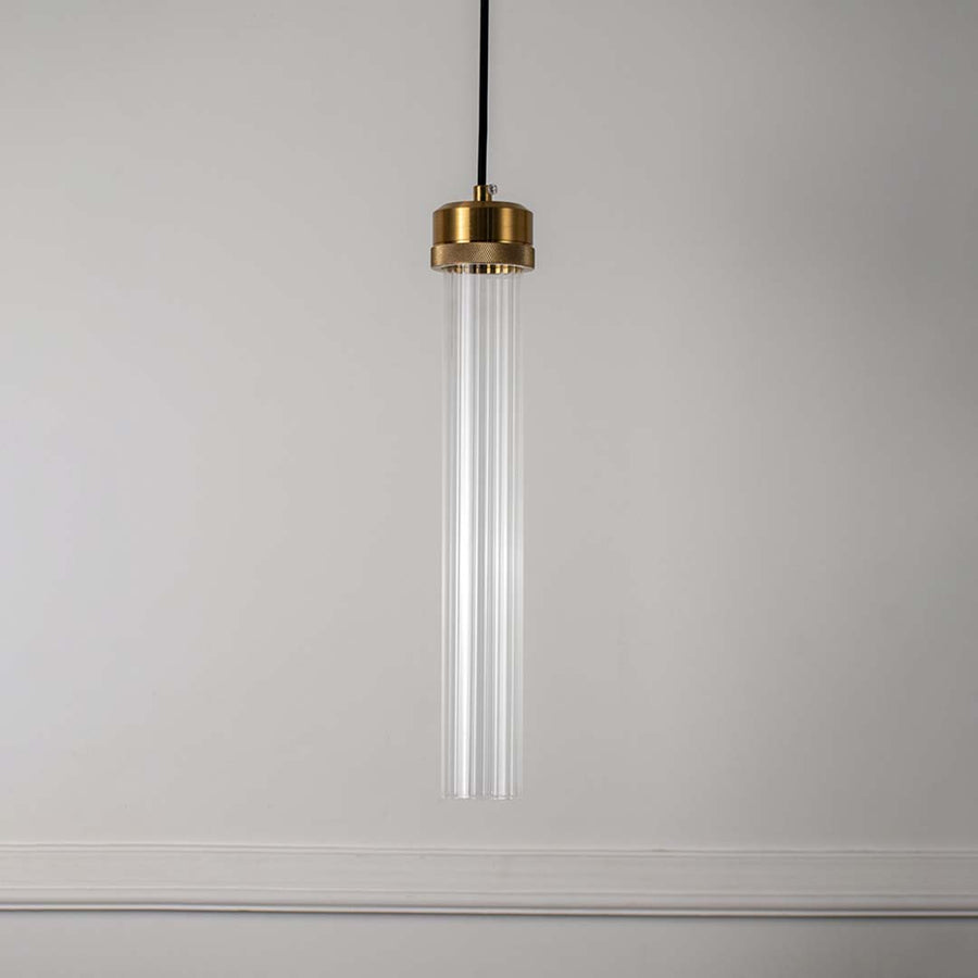 Clear glass tube pendant light with polished brass fittings crafted for elegant modern interiors.