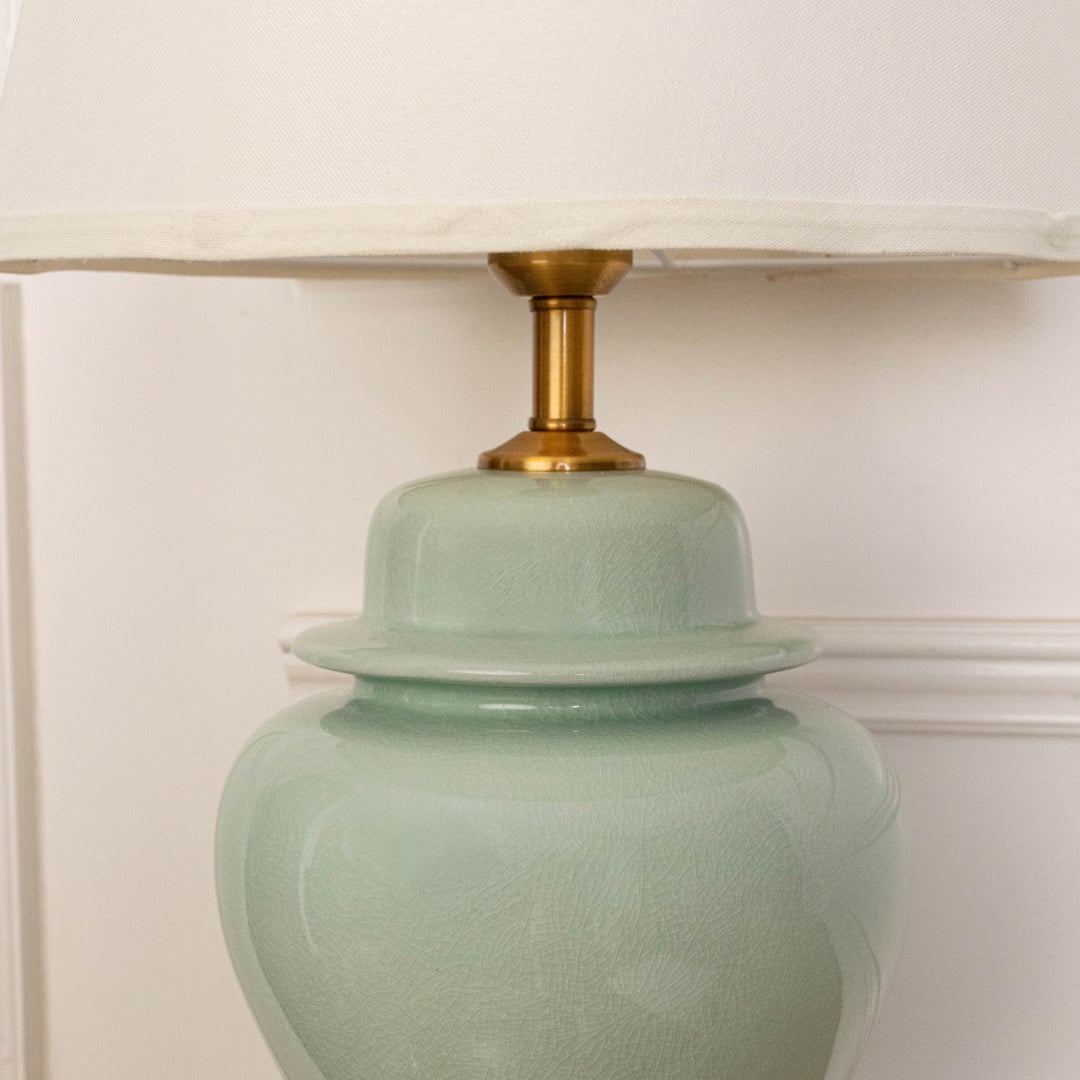 White shade jade green ceramic table lamp on carved console table with light off and white wall background for classic elegant décor.