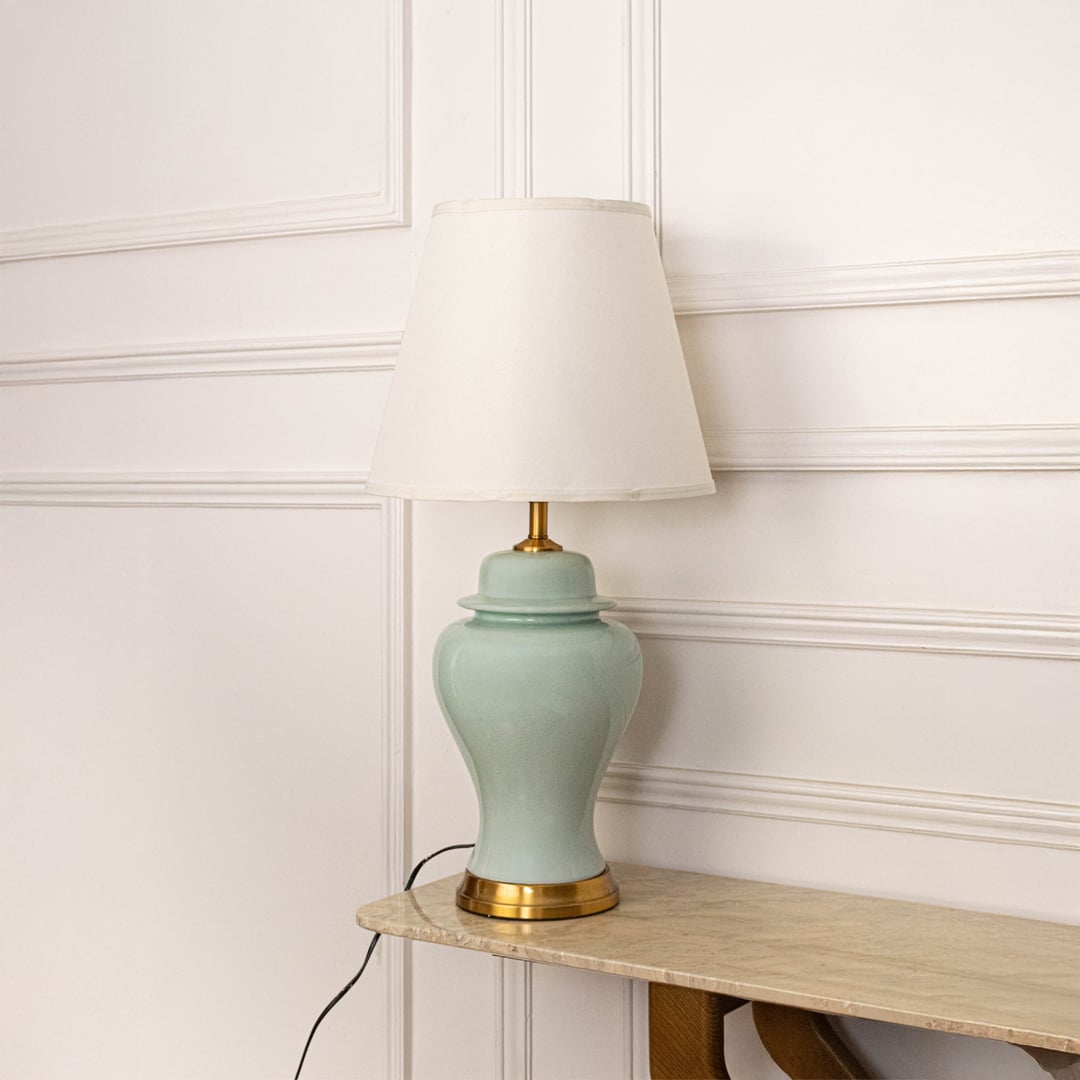 White shade jade green ceramic table lamp on wooden sideboard with light off and white panel wall background for classic elegant décor.