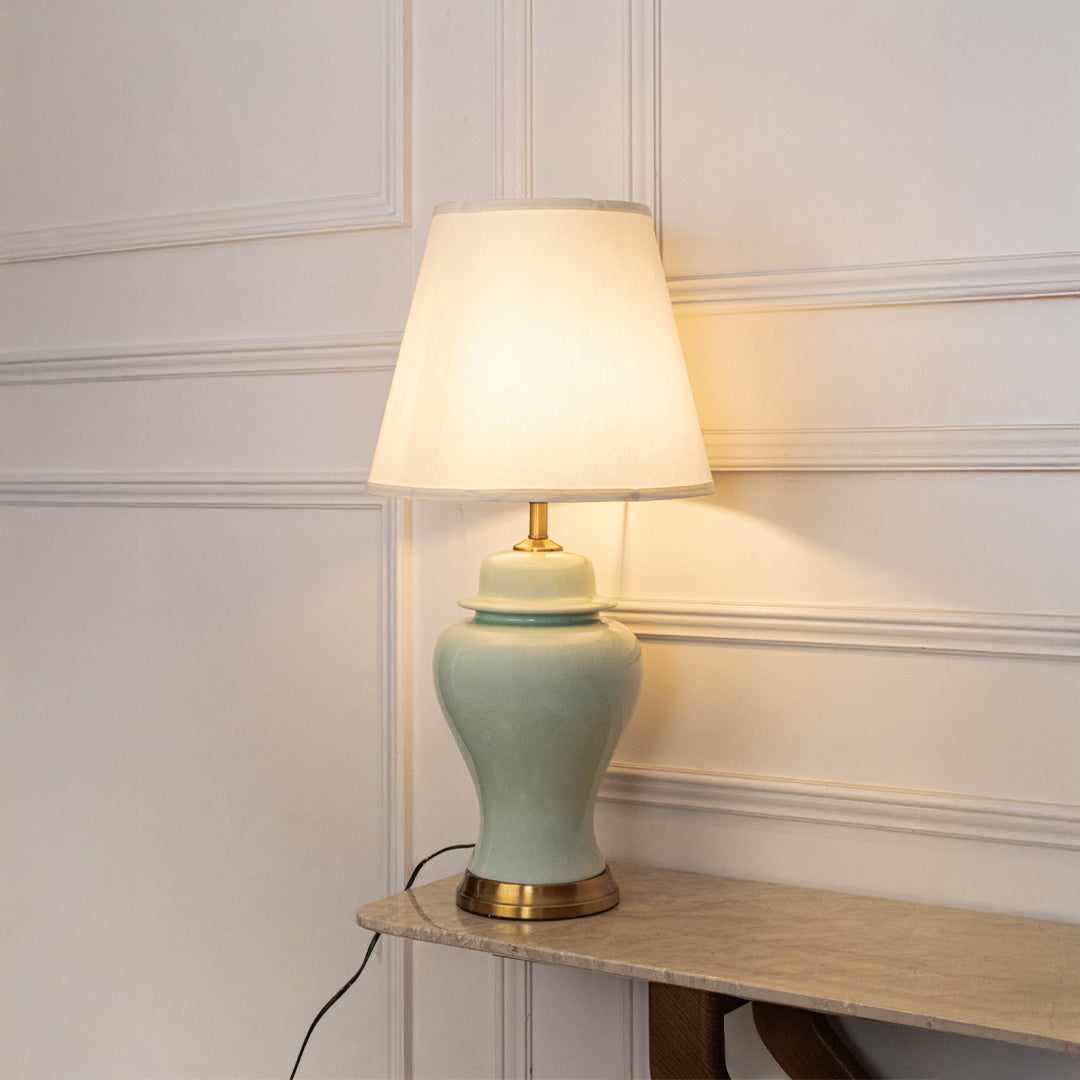Mint green ceramic table lamp with fabric shade placed on a side table creating warm traditional ambient lighting.