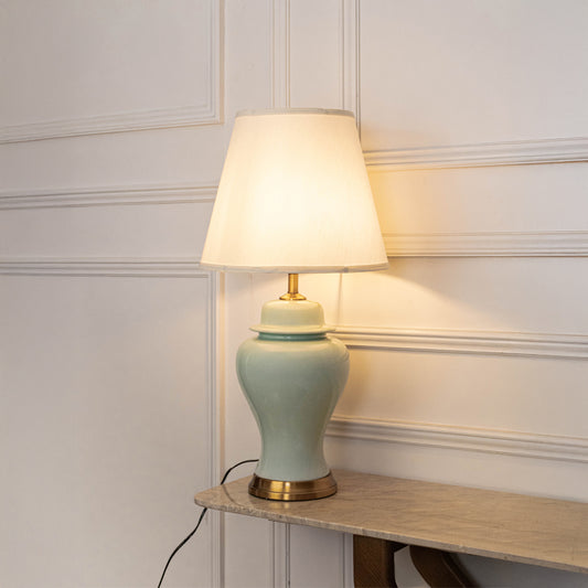 Mint green ceramic table lamp with fabric shade placed on a side table creating warm traditional ambient lighting.