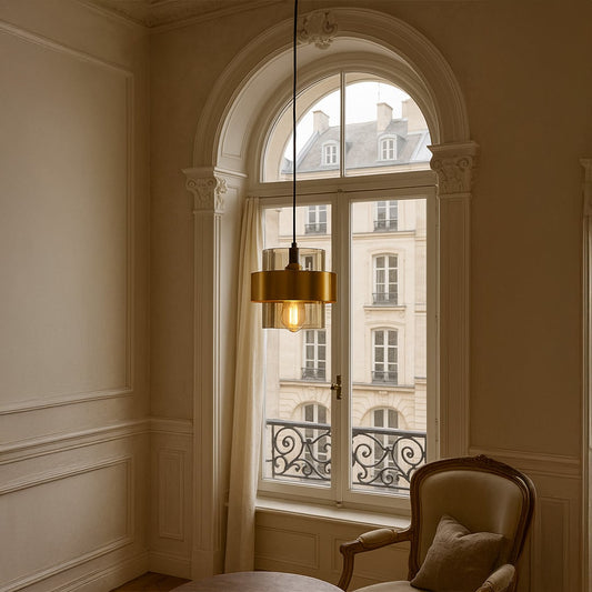 Gold and glass modern pendant light hanging above table adding warm glow to contemporary living room decor.