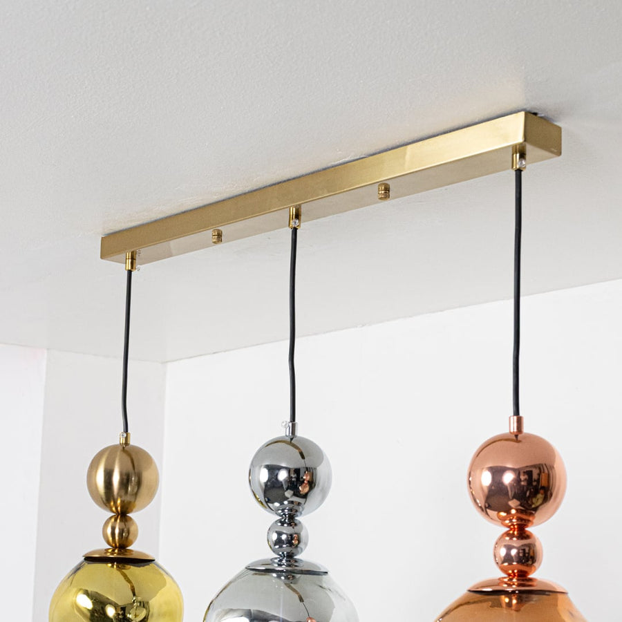 Decorative metallic glass pendant lights with gold ceiling bar for elegant dining room interiors.