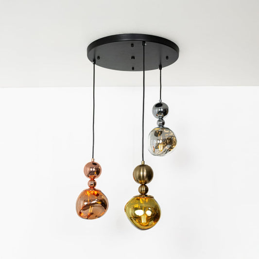 The trio pendant light glowing warmly on a white background with metallic chrome gold and copper shades creating a radiant look.