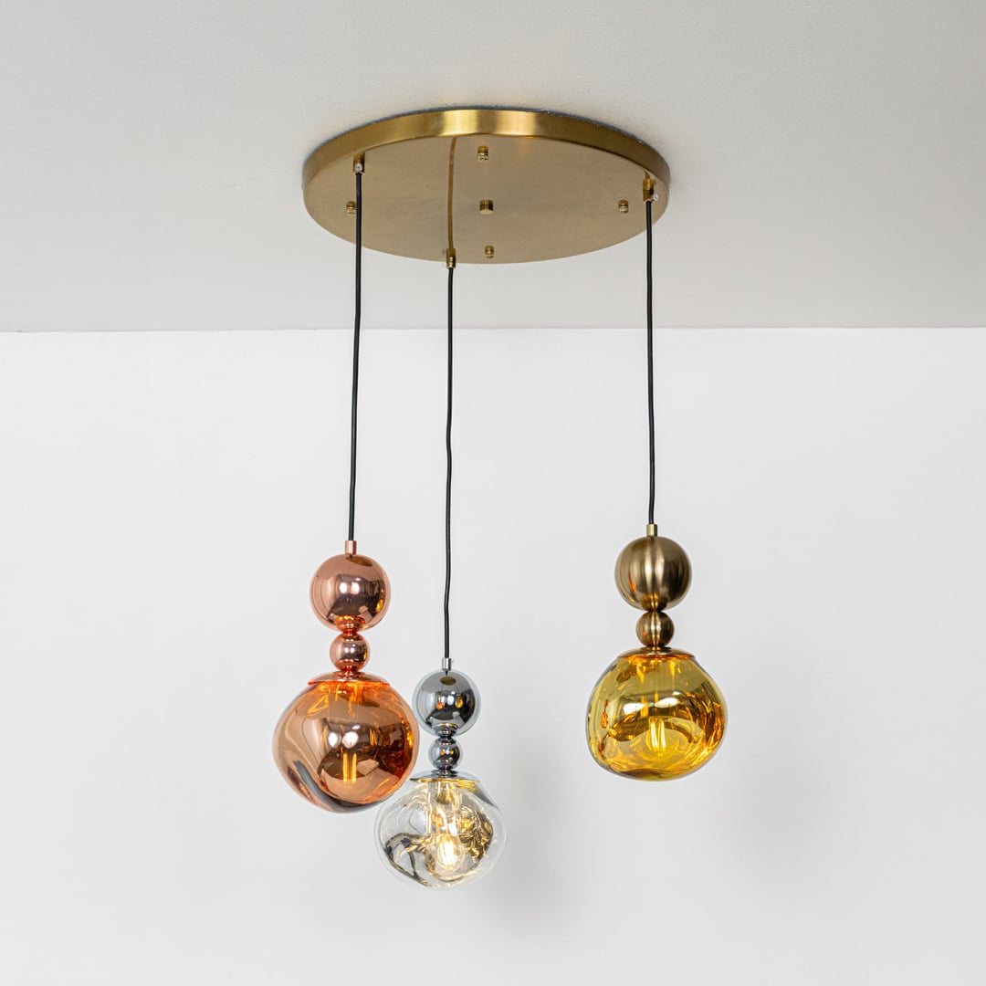 Gold chrome and copper pendant lights glowing softly on a white background creating warm ambient lighting with a modern decorative look.