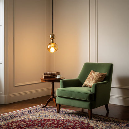 Glass pendant light with metal fitting hanging beside green armchair adding warm ambient lighting and elegant accent to modern living room decor.