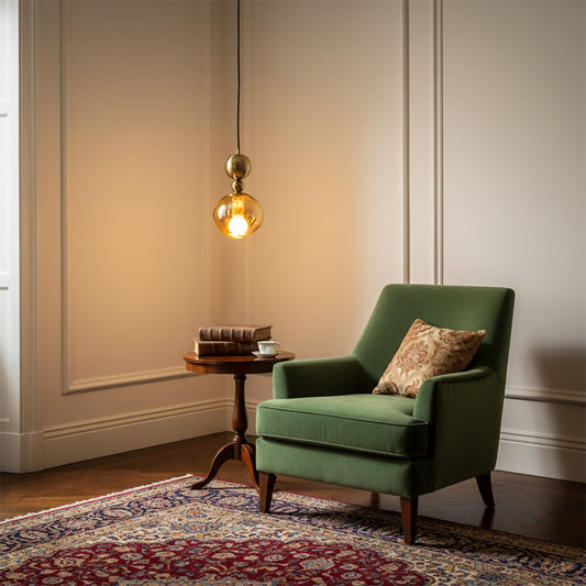 Glass pendant light with metal fitting hanging beside green armchair adding warm ambient lighting and elegant accent to modern living room decor.