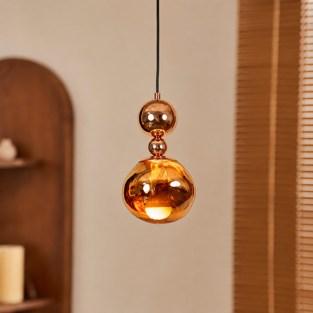 A modern pendant light with a glossy, metallic copper-colored glass shade and a double-sphere design, hanging in a warm, softly lit room.