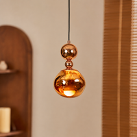 A modern pendant light with a glossy, metallic copper-colored glass shade and a double-sphere design, hanging in a warm, softly lit room.