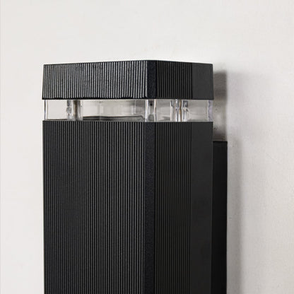 Closeup view of black metal wall light showing ribbed surface finish and clear glass diffuser for premium modern lighting design.
