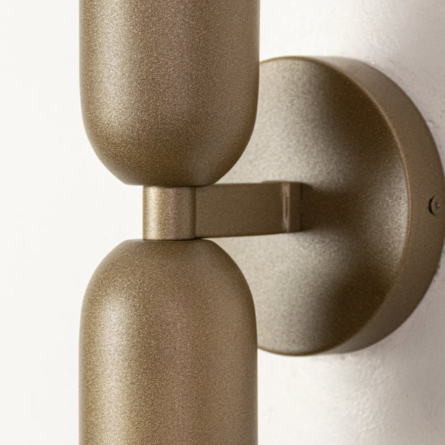 Closeup of gold metal wall light mount showing smooth matte finish solid arm connection and refined modern lighting detail.