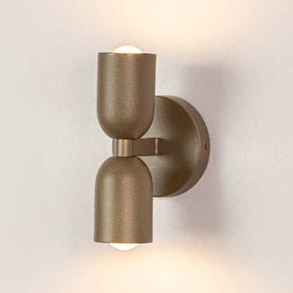 Modern wall light with cylindrical gold metal body displayed on white background offering warm accent lighting for contemporary interiors.