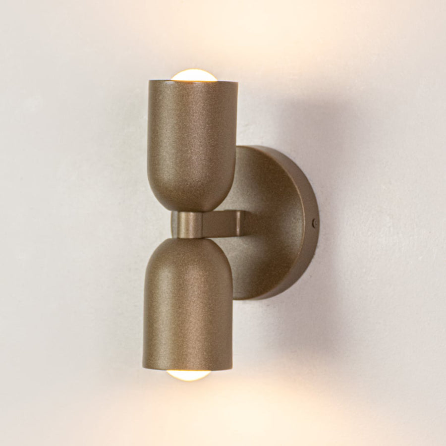 Modern wall light with cylindrical gold metal body displayed on white background offering warm accent lighting for contemporary interiors.