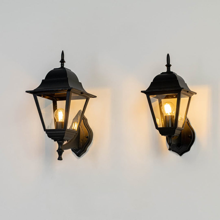 Black metal and glass outdoor wall lantern lights grouped on white background glowing warmly for porch entryway decor Light on white BG.