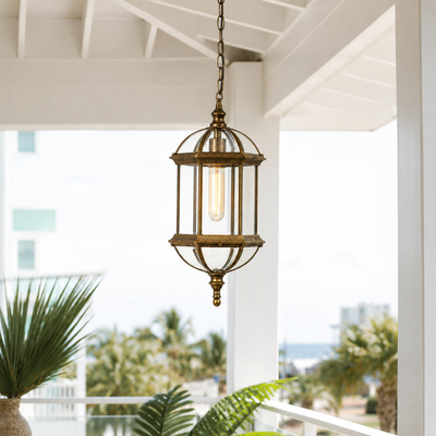 Vintage brass metal open cage glass cylinder hanging lantern pendant light from white porch ceiling for coastal patio styling.