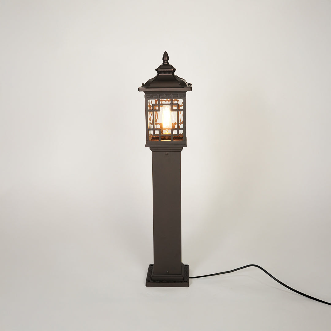 Vintage style outdoor bollard light with black metal frame and clear glass panels on neutral background perfect for garden or driveway lighting.