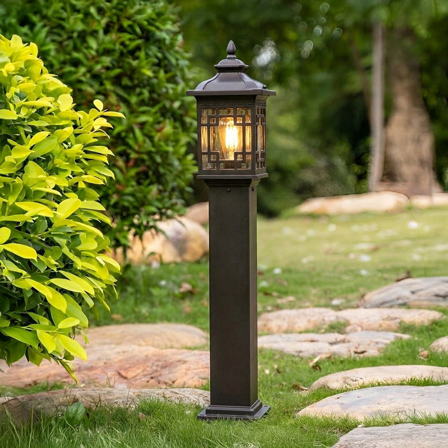 Black outdoor garden pole light with classic lantern design installed along pathway with greenery ideal for landscape lighting.