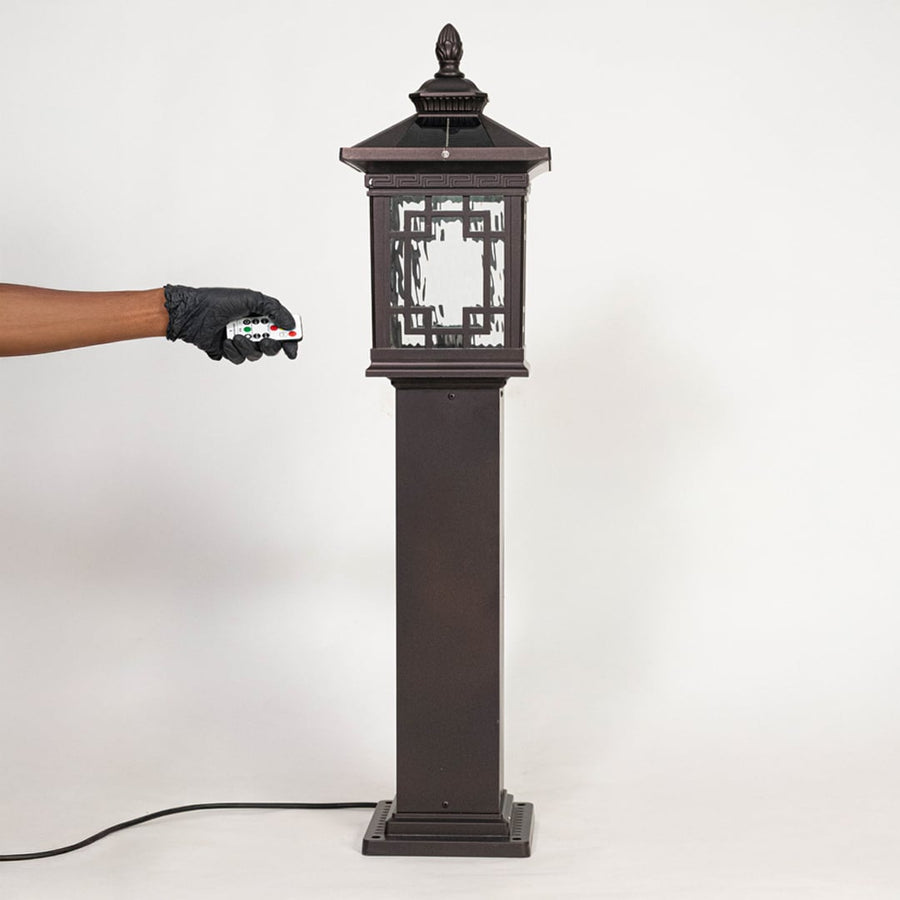 Tall black outdoor pillar lamp post with decorative glass panels shown off on white background surface.