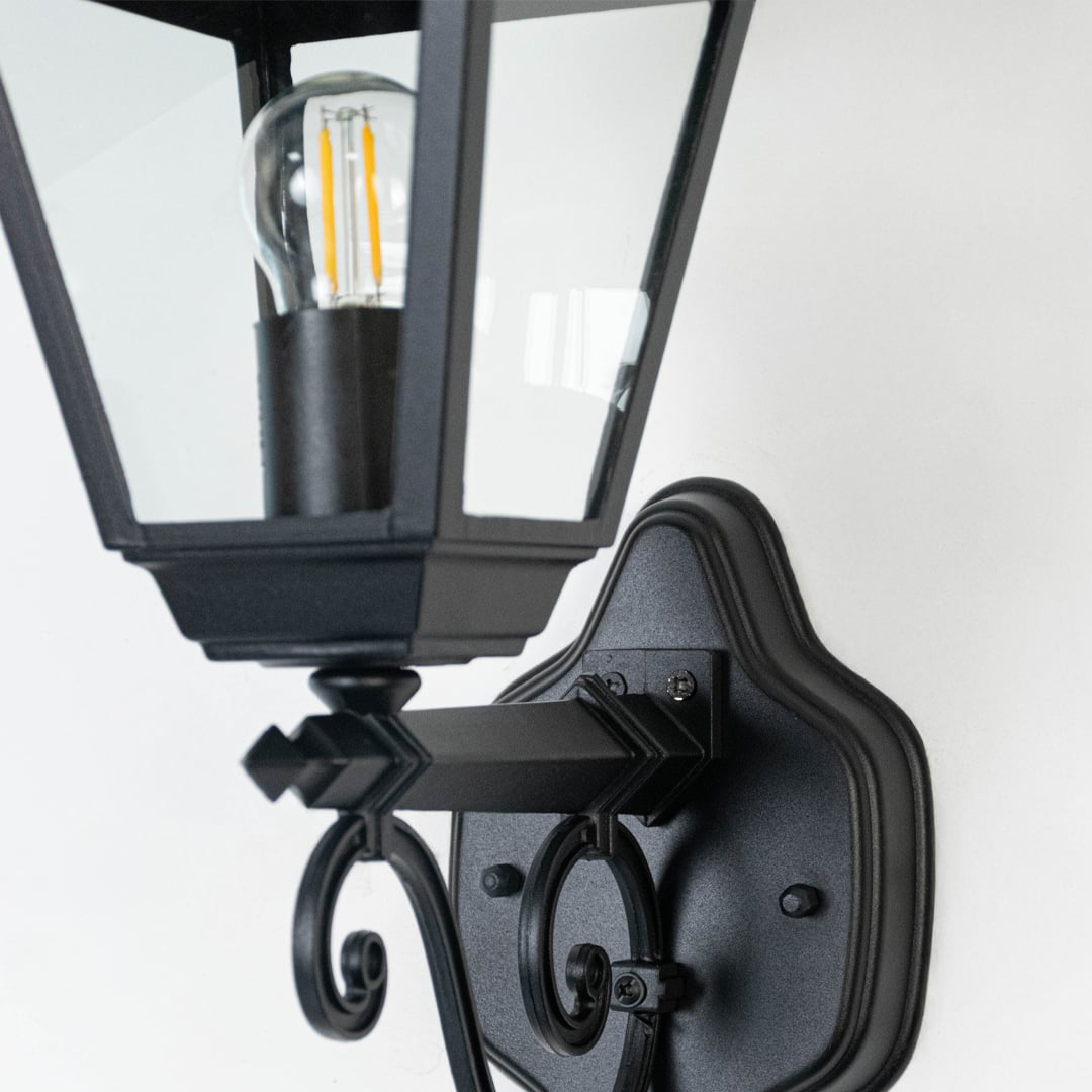 Detailed closeup of outdoor wall lantern highlighting black matte finish  vintage top design  and clear glass sides.