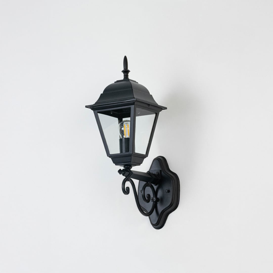 Elegant black outdoor wall lantern unlit on white background showing detailed metal frame and clear glass body in focus.