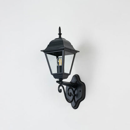Elegant black outdoor wall lantern unlit on white background showing detailed metal frame and clear glass body in focus.