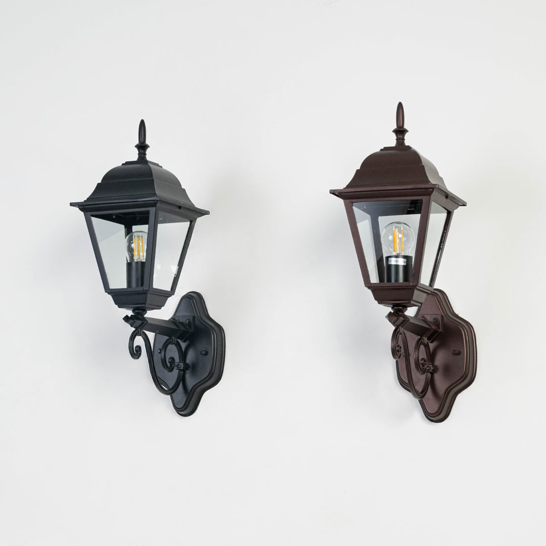 Black metal exterior wall lantern switched off on white background showcasing classic shape and decorative mounting arm.