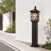 Decorative black iron grid column post lantern light on white gravel path next to concrete driveway for modern home exterior.