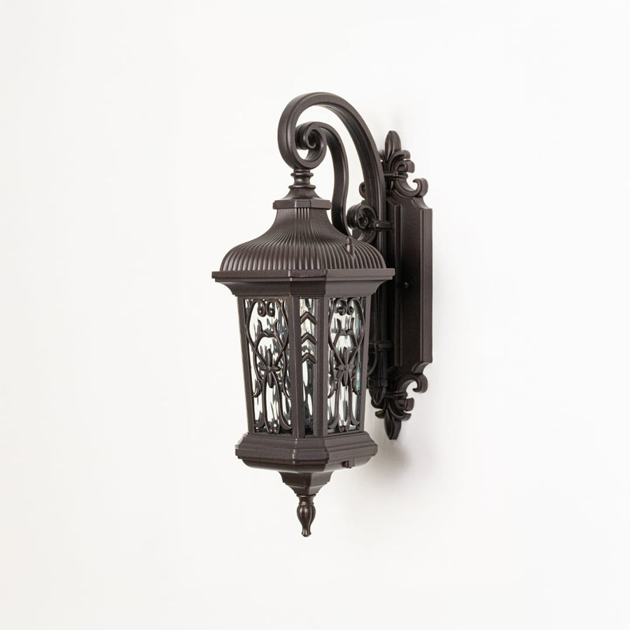Antique bronze metal exterior sconce featuring decorative filigree and glass on a seamless clean white background.