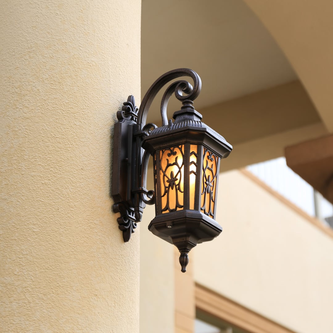 Vintage bronze aluminum outdoor wall lantern glowing on a classic stucco pillar placement outdoor lifestyle image.