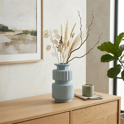 Light blue ceramic decorative flower vase placed on wooden cabinet with dried flowers modern living room home decor styling idea.