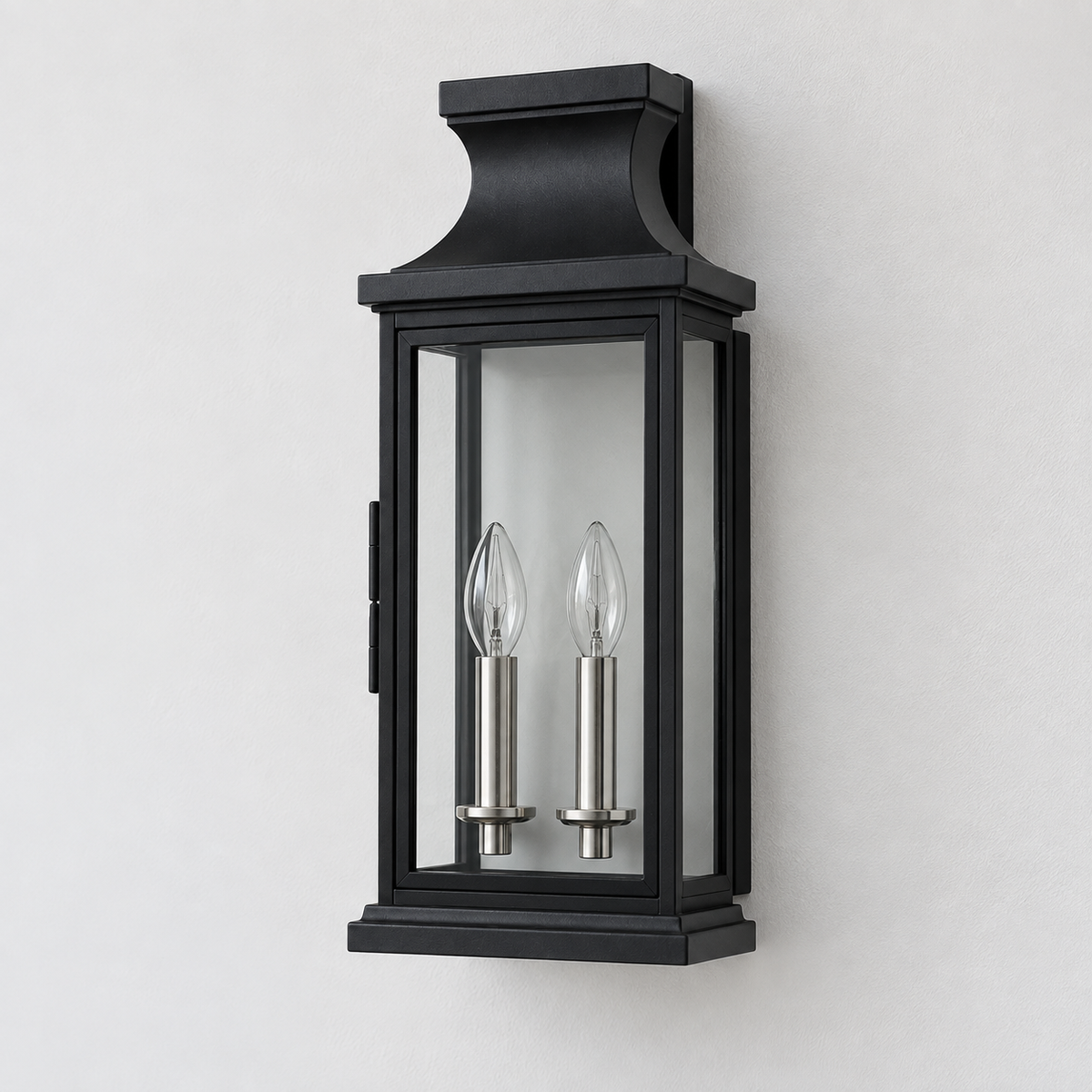 A black outdoor wall sconce with two candle-style bulbs inside, mounted on a light gray wall.