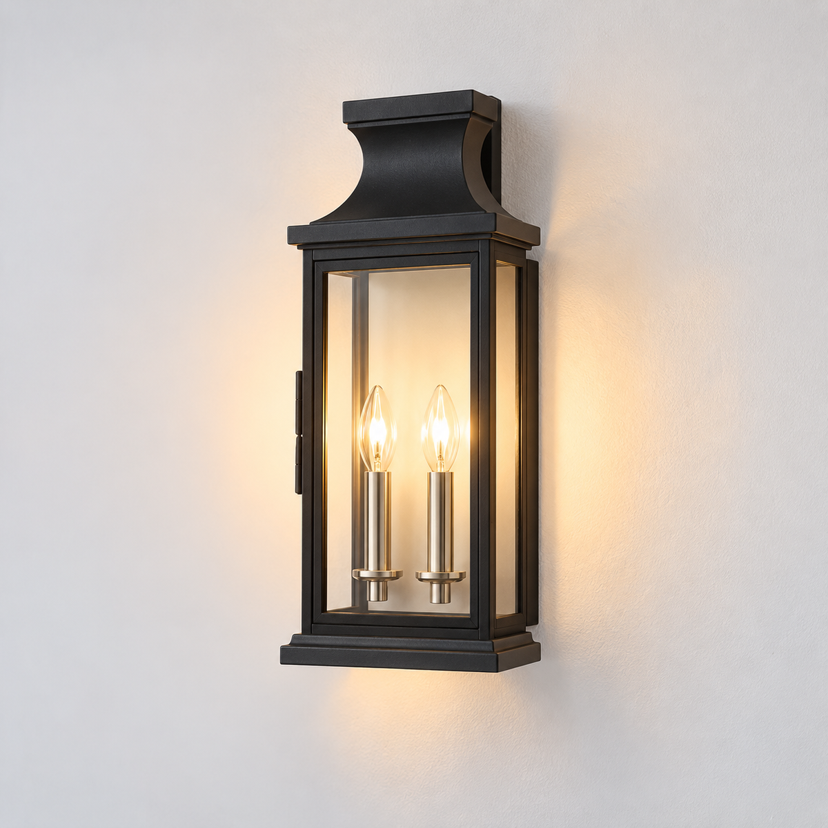 A black lantern-style wall sconce with two lit candle-style bulbs, mounted on a plain light wall.