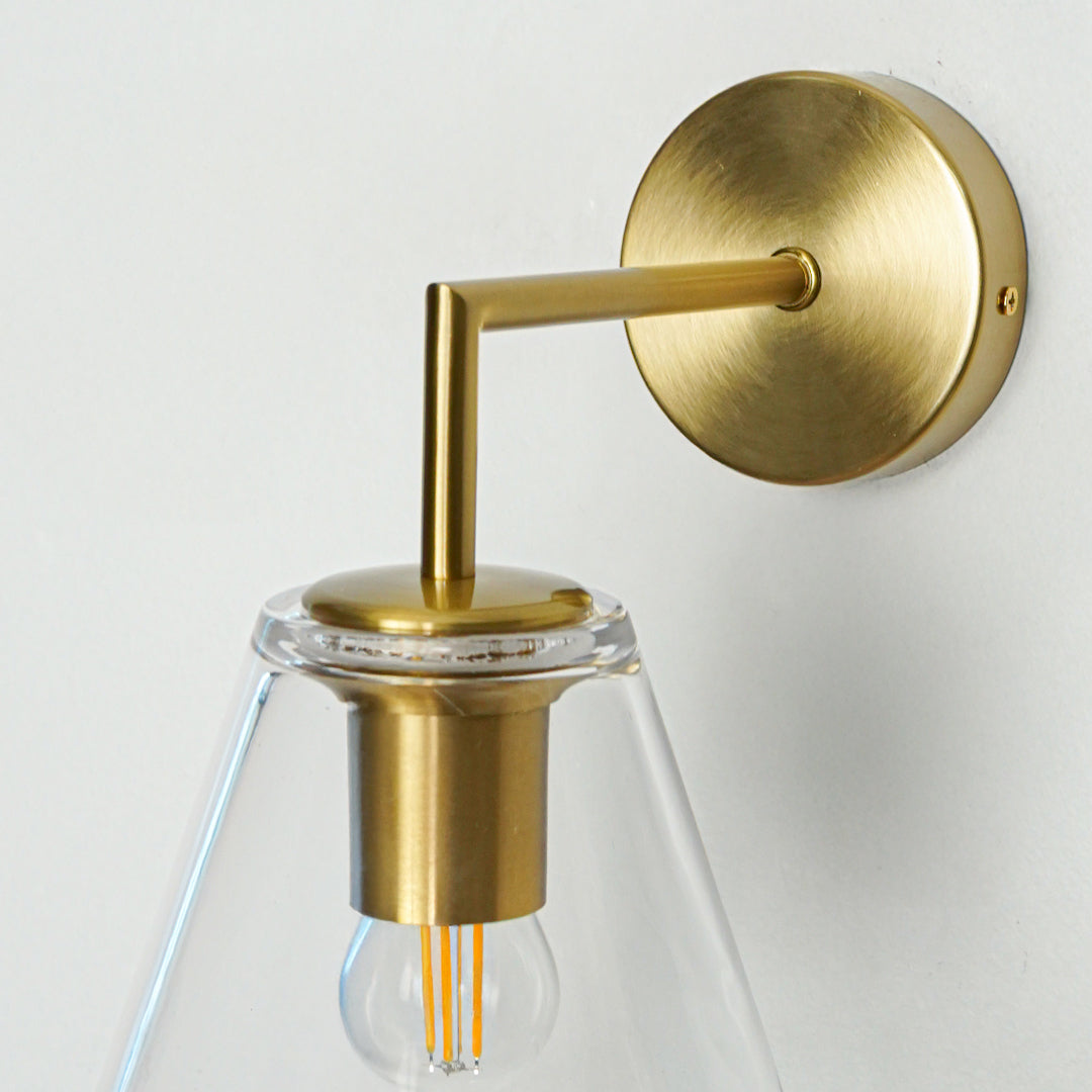 Elegant brass wall light with clear cone glass shade for stylish modern bedroom and hallway decor.