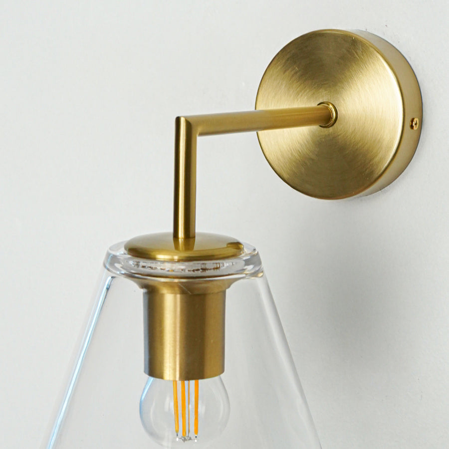 Elegant brass wall light with clear cone glass shade for stylish modern bedroom and hallway decor.
