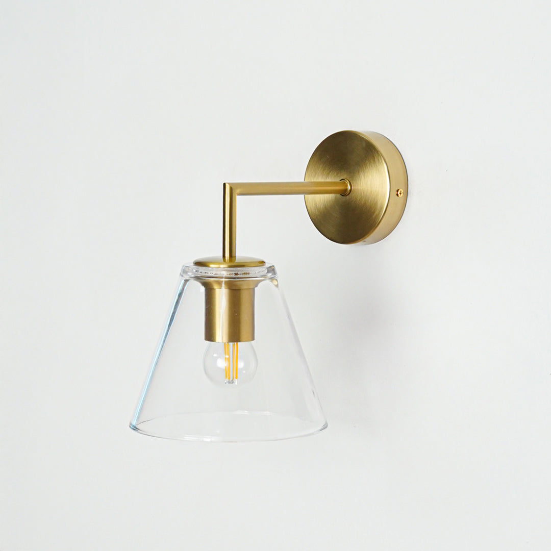 Modern brass wall light with clear cone glass shade for stylish bedroom and hallway decor.