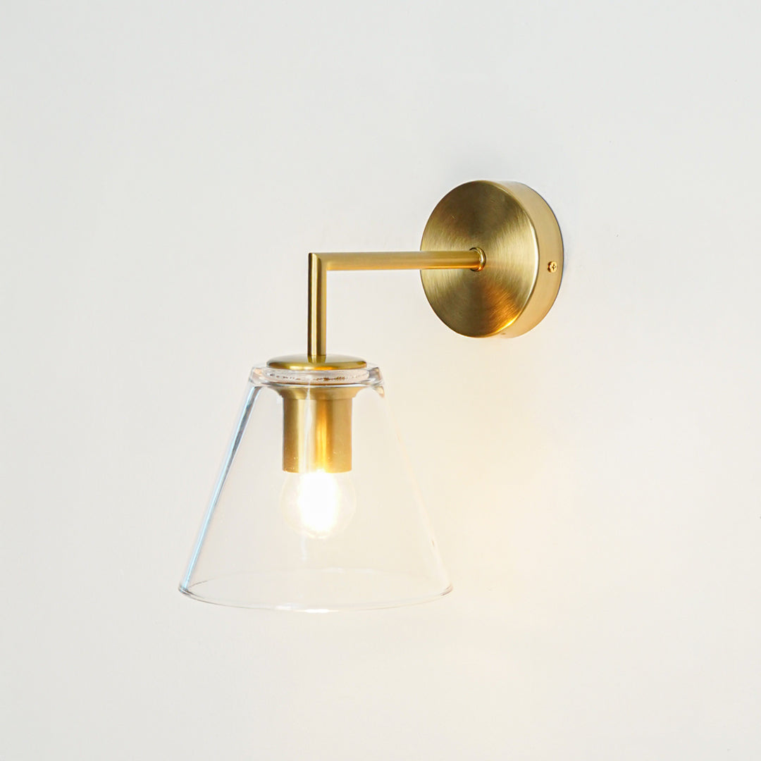 Contemporary brass wall light with clear glass shade creating warm elegant interior lighting decor.