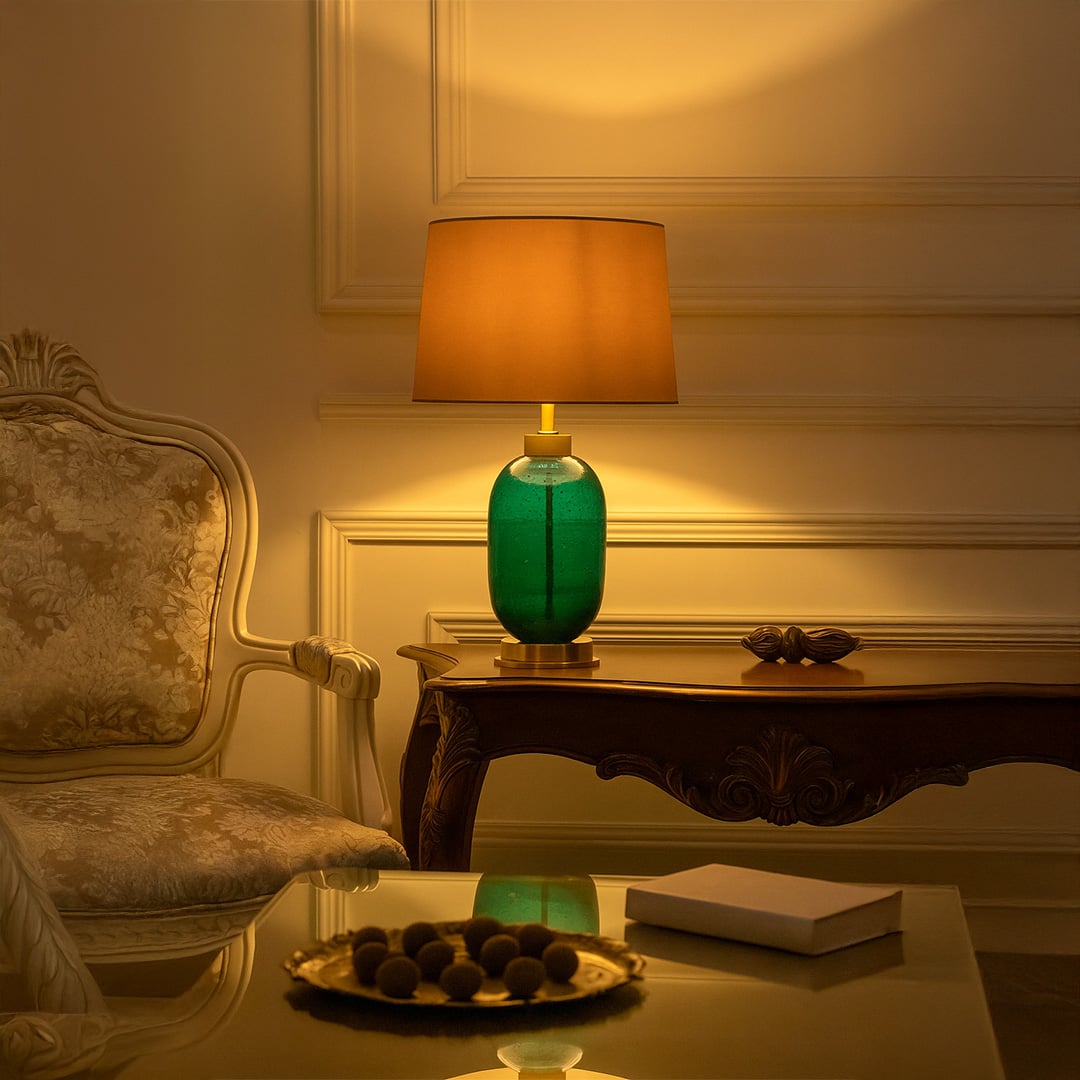 Green ceramic lamp on side table with light on and sofa background for vibrant elegant décor.