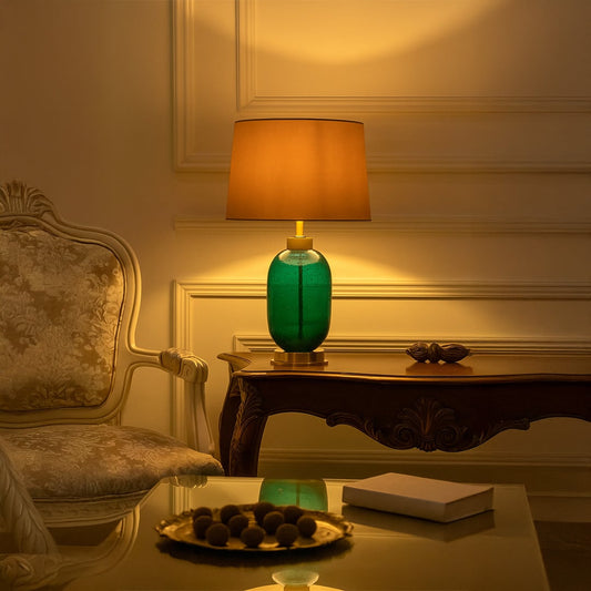 Green ceramic lamp on side table with light on and sofa background for vibrant elegant décor.