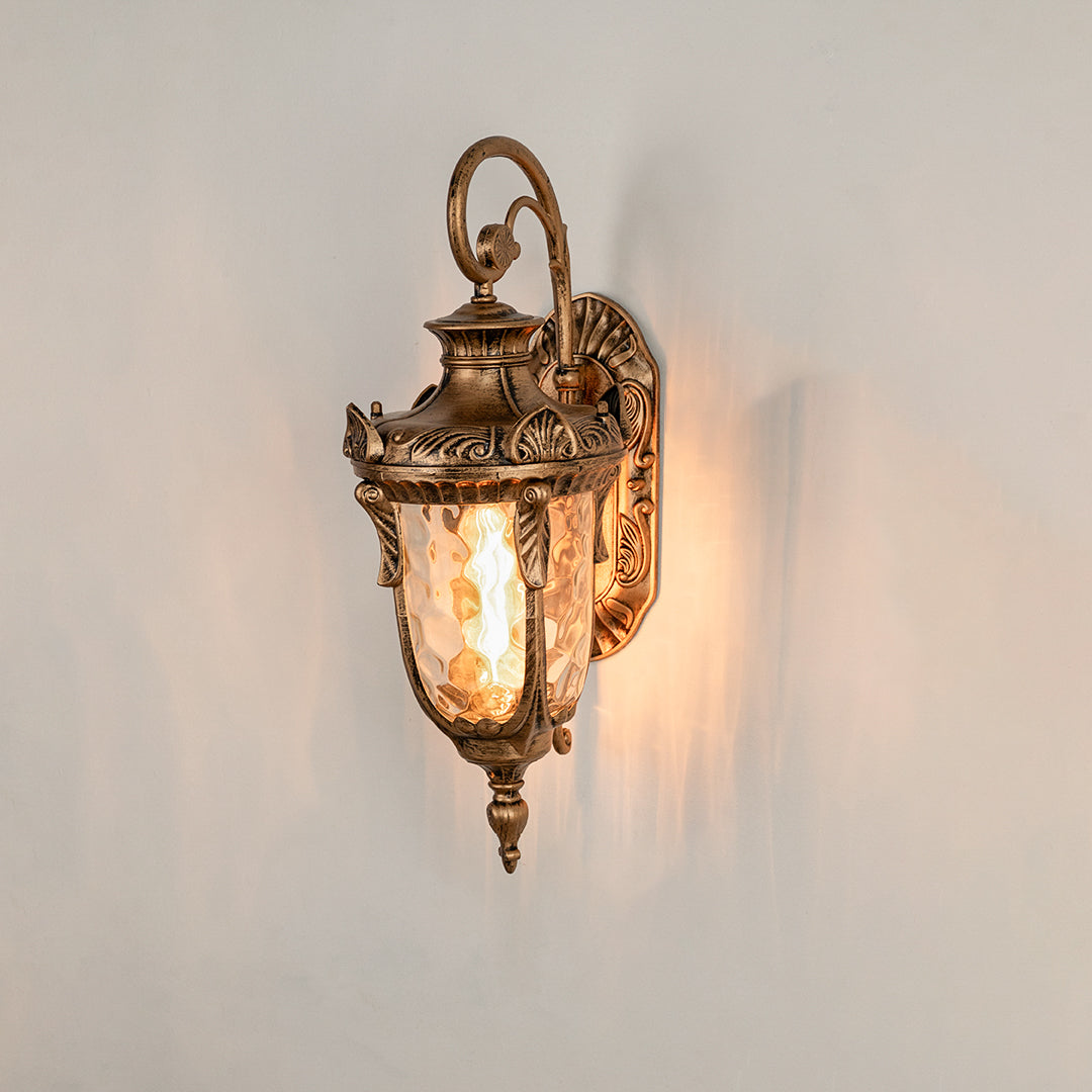 Antique brass metal outdoor wall light on white background with textured water glass shade for elegant porch decor.