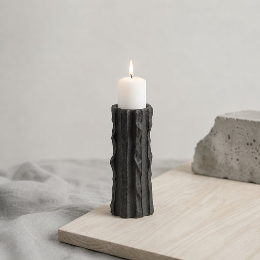 Black textured candle holder with white candle placed on table for modern contemporary decor styling.