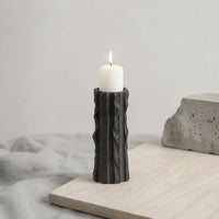 Black textured candle holder with white candle placed on table for modern contemporary decor styling.